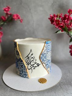 there is a small cup with arabic writing on it next to some flowers and a vase