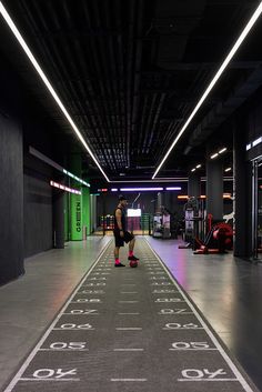 a man is walking down an indoor parking garage area with neon lights on the ceiling