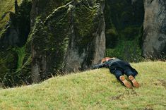 a person laying on top of a lush green hillside next to a cliff face covered in moss