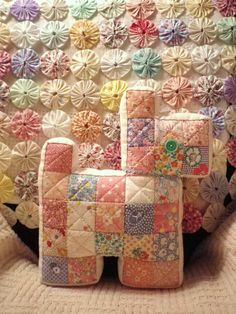 a quilted wall hanging on the side of a bed covered in colorful fabric flowers