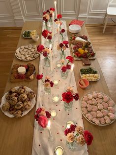 a long table covered in plates and bowls filled with food next to candles on top of a wooden floor