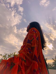 a woman with long hair wearing an orange sari and looking up into the sky