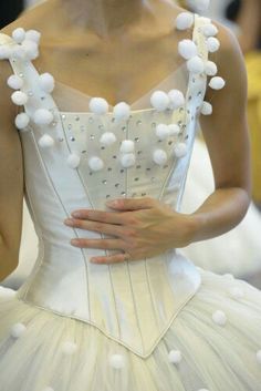 a woman wearing a white dress with pom - poms on it