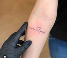 a person with a tattoo on their arm holding up a glove that has the word love written in cursive writing