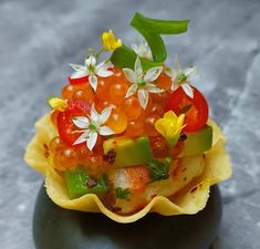 a close up of a fruit and vegetable dish on a black rock with flowers in it