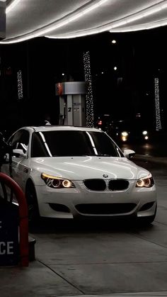 a white car is parked in front of a gas pump at night with lights on