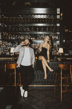 a man and woman sitting at a bar with bottles on the wall behind them,