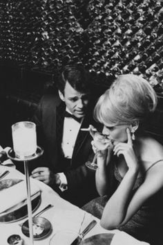 a man and woman sitting at a table with food in front of them while talking on the phone