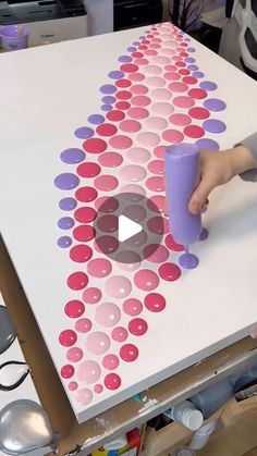 a person is painting on a table with polka dot designs and holding a purple cup