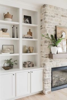 a living room with white bookcases and a fire place in the corner, next to a stone fireplace