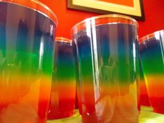 three rainbow colored cups sitting on top of a table next to each other in front of a red wall