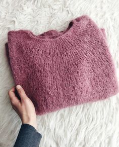 a hand holding a pink sweater on top of a white rug