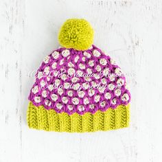 a pink and yellow knitted hat with flowers on it sitting on a white surface