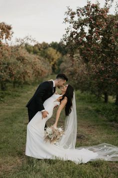 a bride and groom kissing in an apple orchard