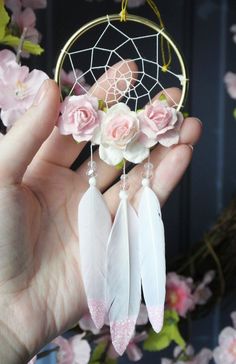 a hand holding a white dream catcher with pink flowers on it and roses in the background