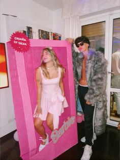 two people dressed in costumes standing next to a pink box with the word barbie on it