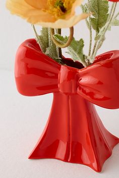 a red vase with flowers in it on a white tableclothed surface and the bottom part of the vase is shaped like a bow