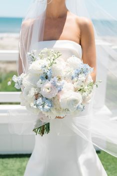 the bride is holding her wedding bouquet by the beach