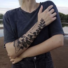 a person with a tattoo on their arm near the water and trees in the background