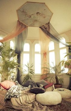 a bed with lots of pillows on top of it in a room filled with potted plants