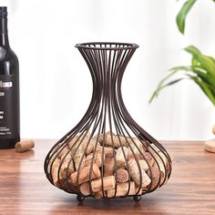 a wine bottle sitting next to a metal vase filled with corks on a wooden table