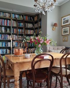 a dining room table surrounded by bookshelves with flowers in vases on it