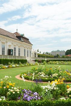 a large white building with lots of flowers in the front yard and around it is a circular garden