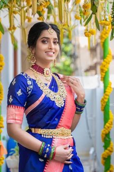 a woman in a blue and pink sari with gold jewelry on her neck posing for the camera