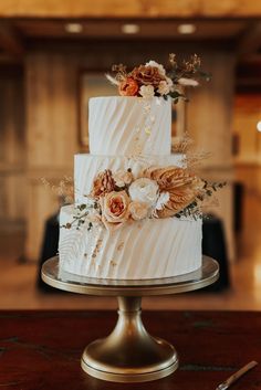 a three tiered white wedding cake with flowers on the top and sides, sitting on a table