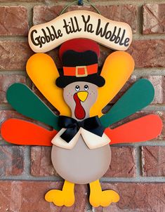 a wooden turkey ornament hanging on a brick wall with a sign that says gobble till to wobble