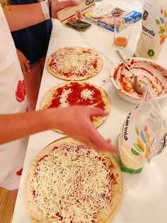 people making homemade pizzas on a table