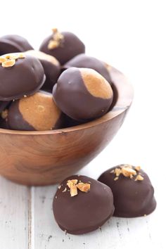 some chocolates are in a wooden bowl on a white table and one is half eaten