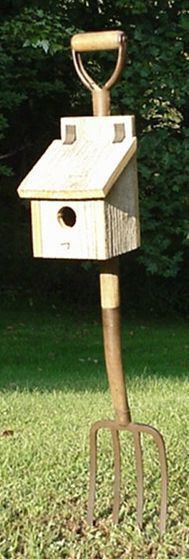 a bird house with a shovel stuck in it's back end on the grass