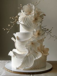 a three tiered white wedding cake with flowers on the top and bottom, sitting on a table