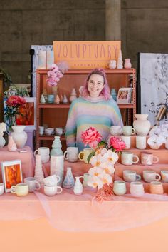 a woman sitting at a table with vases and flowers in front of her on display