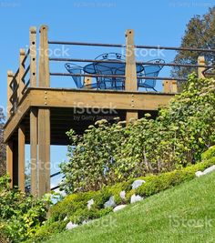 a wooden structure with two blue chairs sitting on it's roof above green grass and bushes