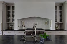 a kitchen with white cabinets and black counter tops, an oven hood over the stove