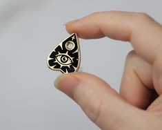 a hand holding a small black and gold brooch with an eye on it's side