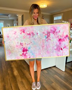 a woman holding up a large painting in her hands