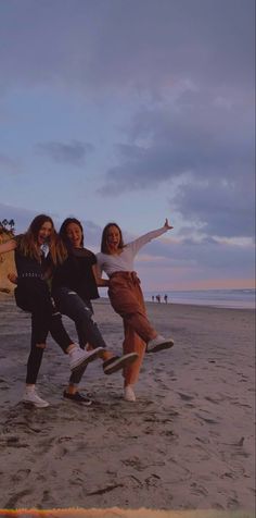 three girls are posing on the beach with their arms in the air and one girl is holding her skateboard