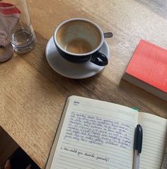 a cup of coffee sitting on top of a wooden table next to an open notebook