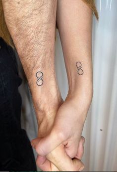 two people holding hands with small tattoos on their arms and wrist, both showing the same symbol