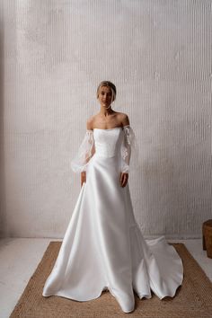 a woman in a white wedding dress standing on a mat with her arms behind her back