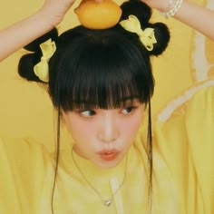 a young woman holding an orange in front of her head while wearing a yellow shirt