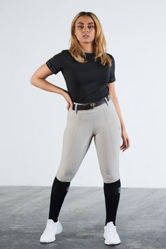 a woman is standing in front of a white wall wearing grey pants and black top