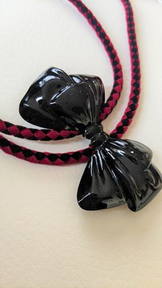 A black shiny bow over red and black velour cord makes this piece pop! Finished off with black enamel tips, you can wear this with any of your punk, rockabilly, goth, combos! 18.5"L, 2"H x 2.75"W, 19g RockaBolos are made with love and incorporate vintage and/or handmade materials.  Please anticipate that each piece will have a story. They have character, a past, and maybe even "imperfections".  But this is wearable art. Who would want it any other way? Black Ribbon Bow For Evening, Black Bow Tie With Decorative Bow For Evening, Black Decorative Bow Tie For Evening, Black Ribbon Bow Tie For Evening, Adjustable Black Bow For Black Tie Events, Black Ribbon Bow For Gifts, Black Bow Tie With Ribbon For Gift, Black Ribbon Bow Tie For Gift, Adjustable Black Bow Tie For Party