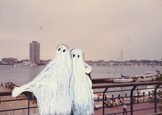 two white ghost statues standing next to each other in front of a body of water