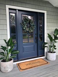 two potted plants are sitting on the porch next to a blue door and welcome mat