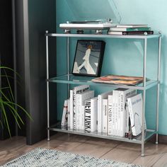 a metal shelf with books and magazines on it in front of a blue painted wall