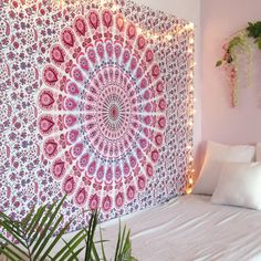 a bed with a pink and blue tapestry on the wall next to pillows in front of it